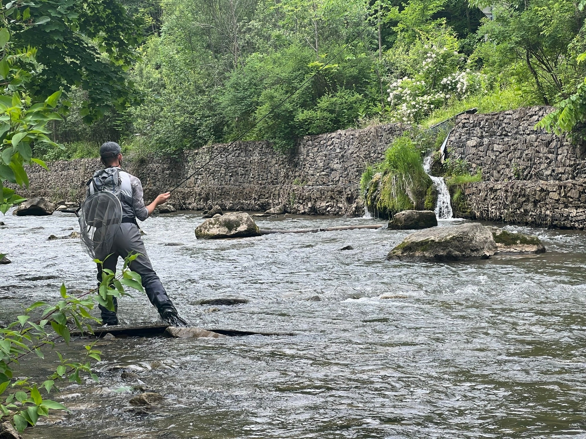 An angler with his back turned, fly fishing in a shallow river.