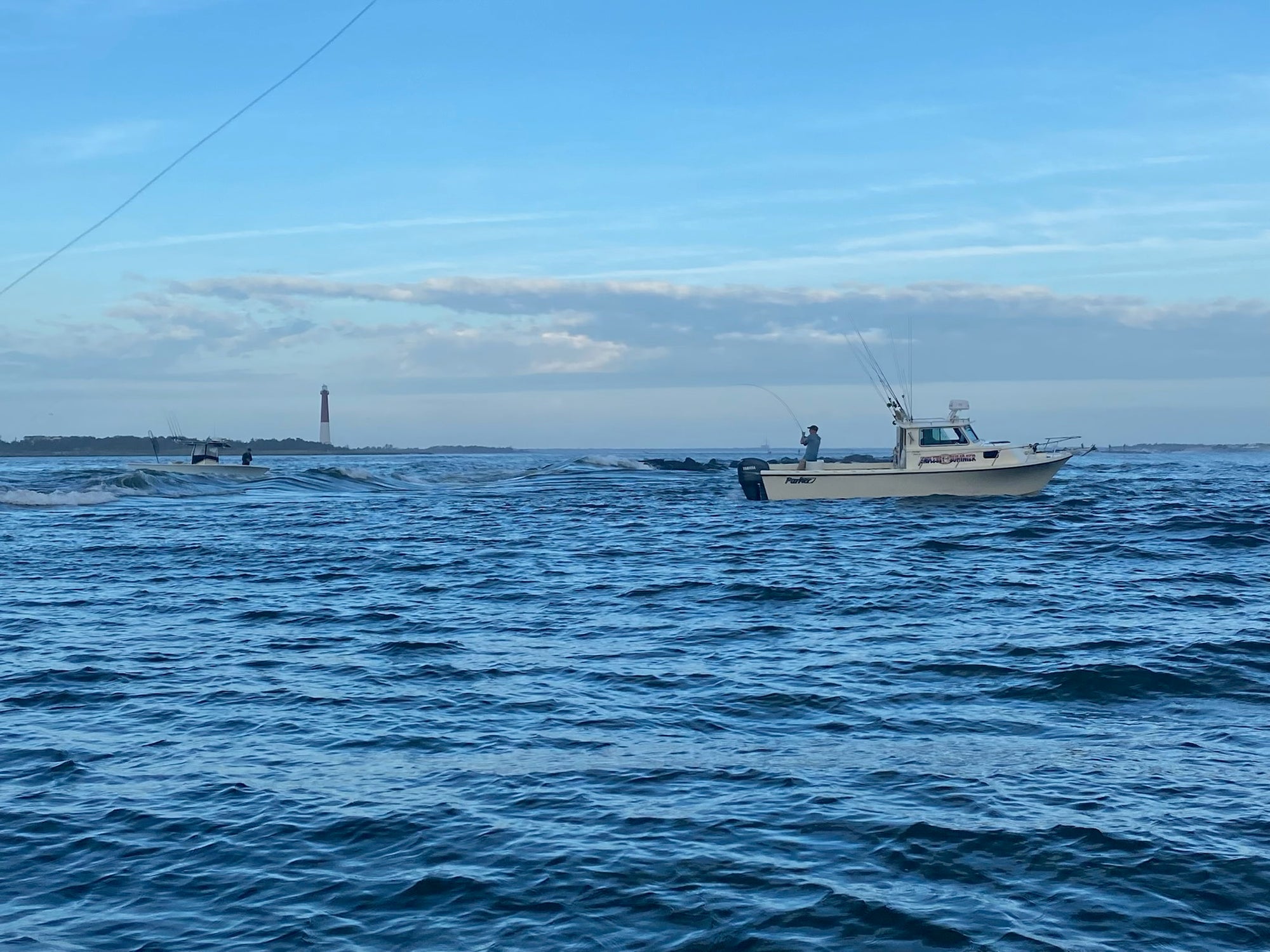 Two boats are on the water with a lighthouse in the background 