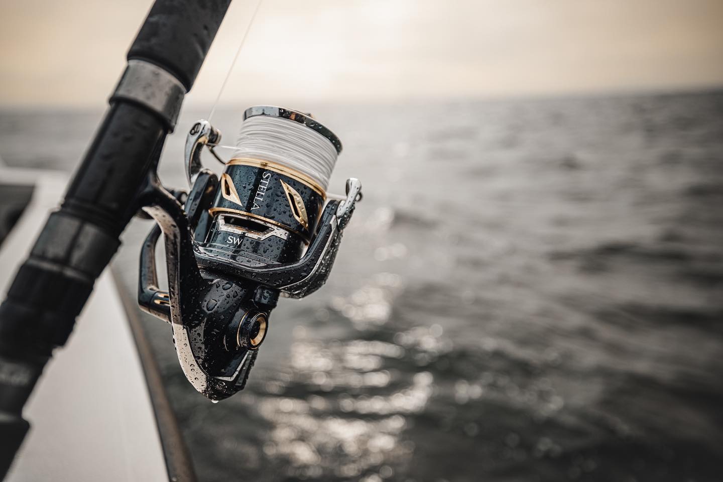 Closeup shot of a fishing reel and pole on a boat, with water in the background