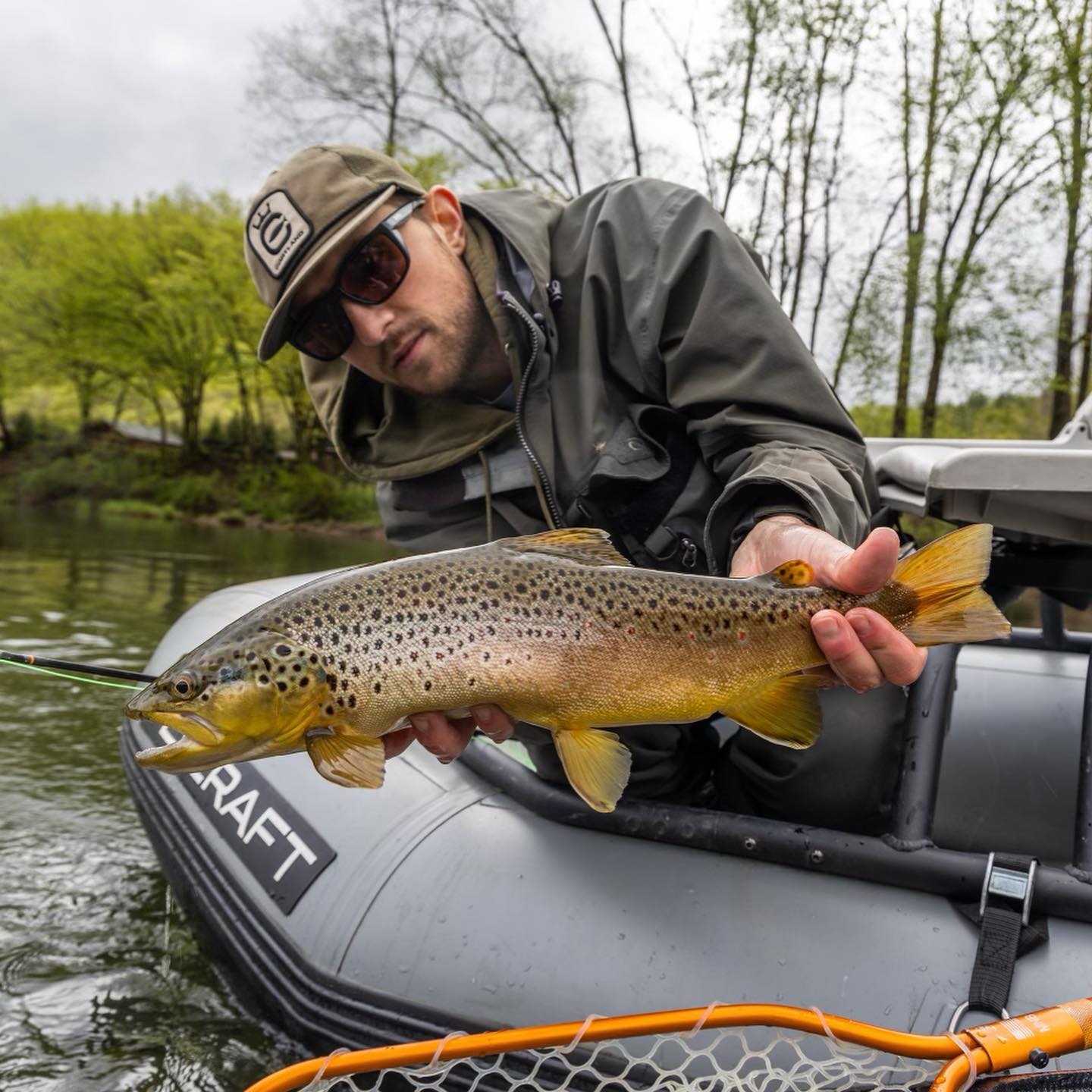 An angler is leaning over a boat and holding onto a fish he caught