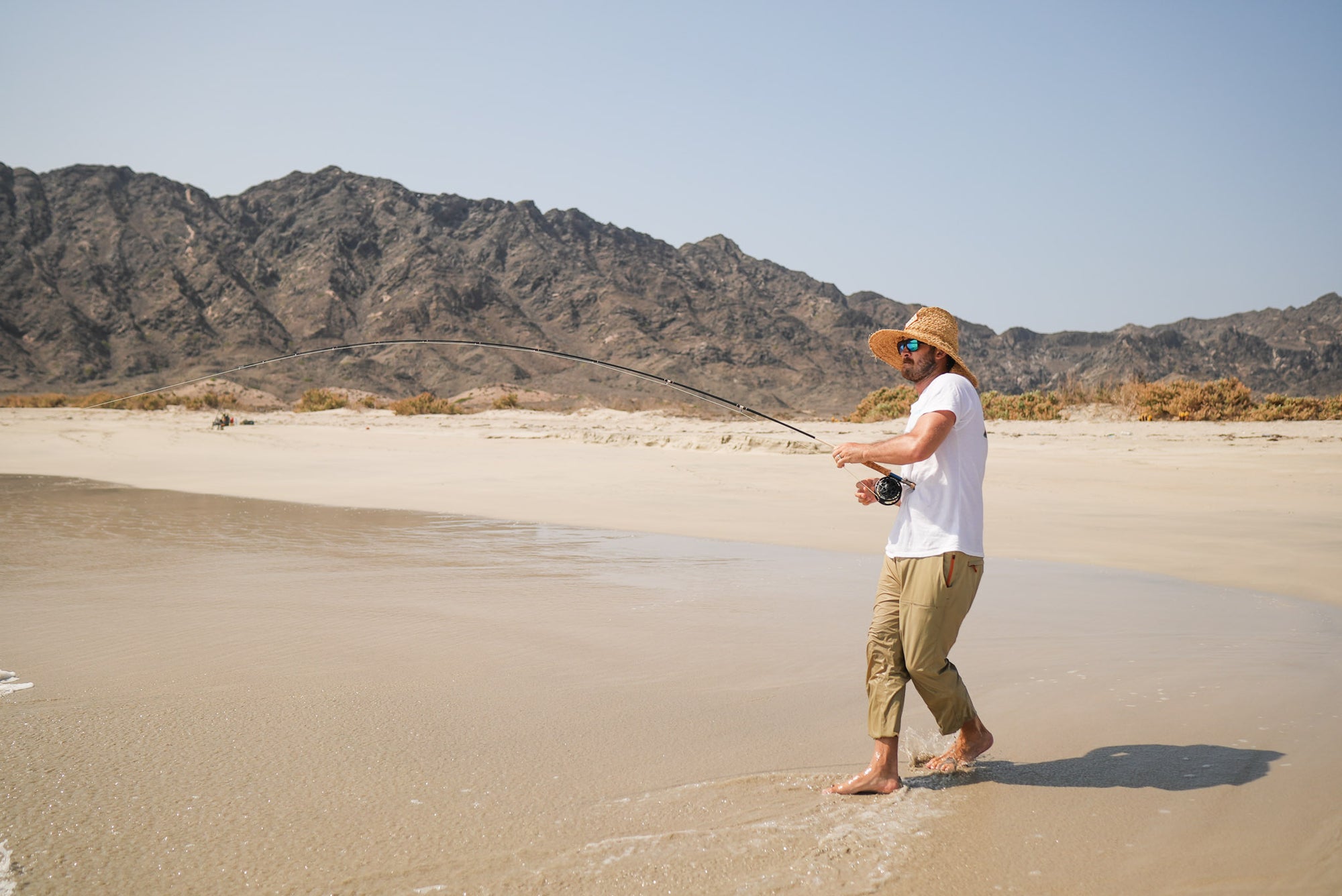 An angler is standing on a beach and reeling in his fishing line