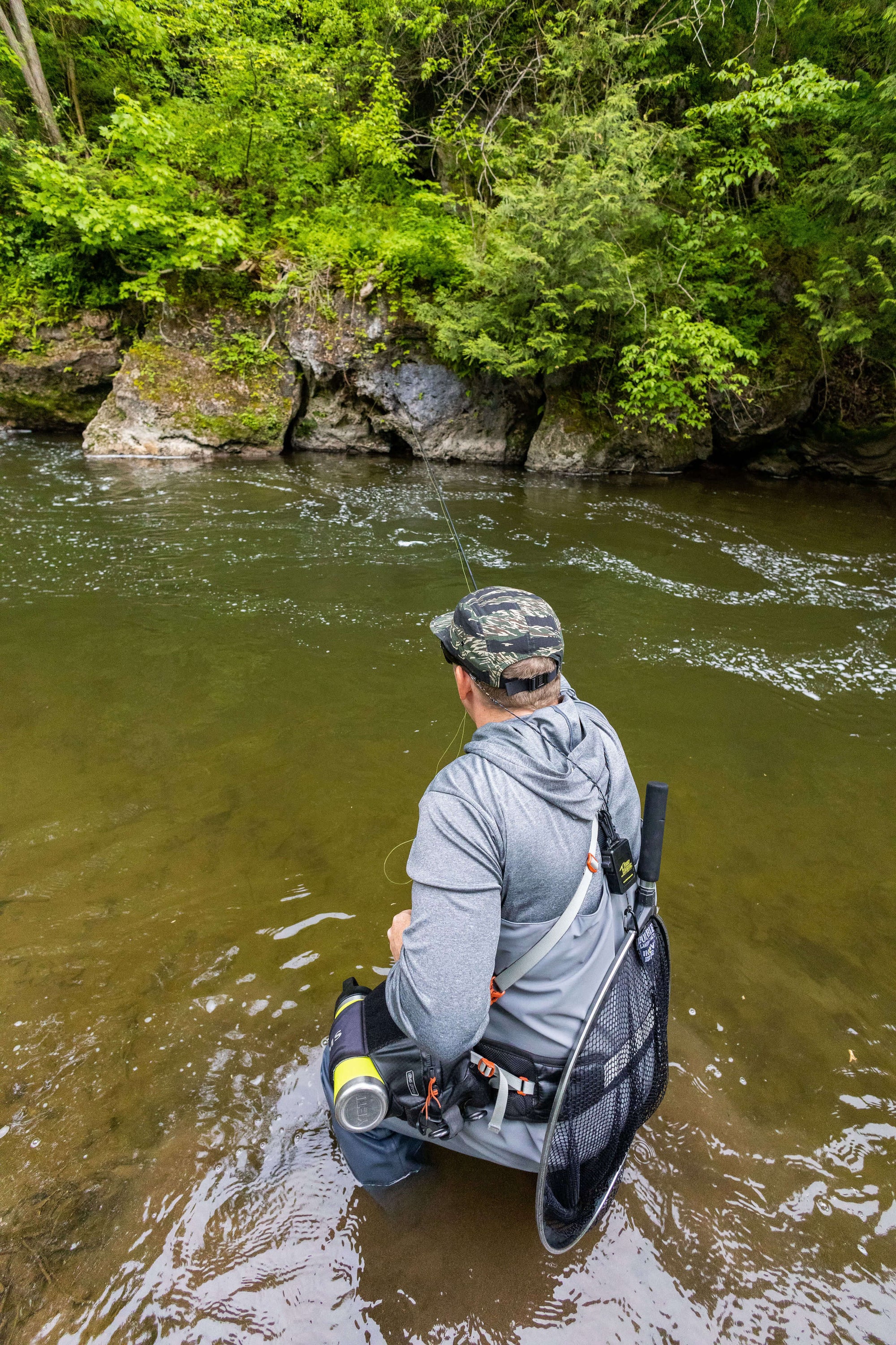 Angler is wearing the Cortland Jungle Cap and is fly fishing. His back is towards the camera and is standing in waste high water. 