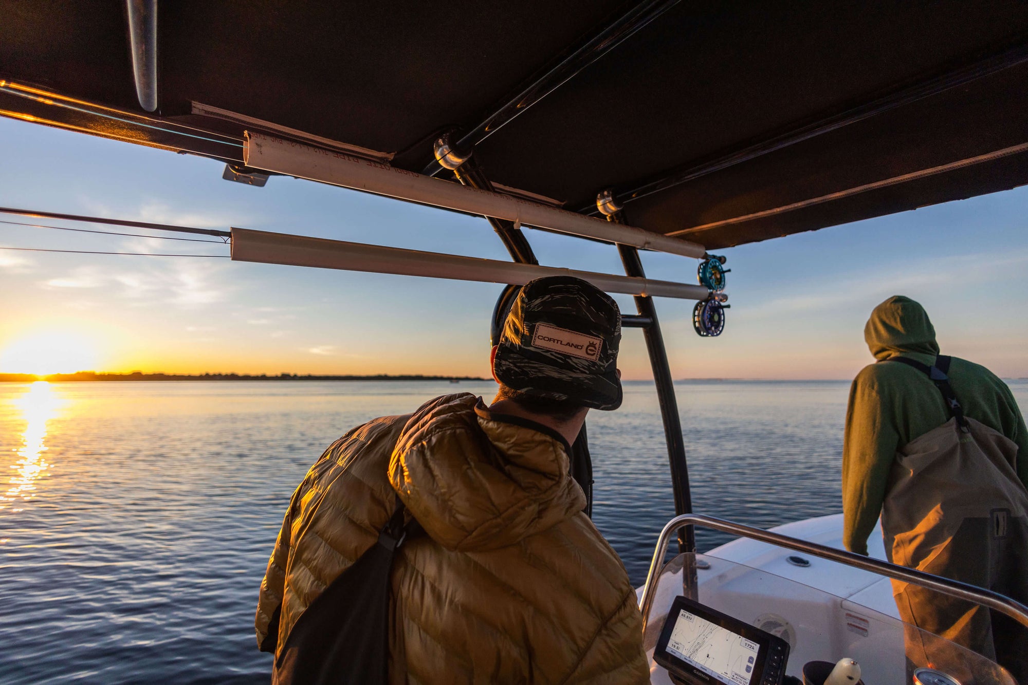 Two fishermen are standing on a boat and overlooking the sunset. 