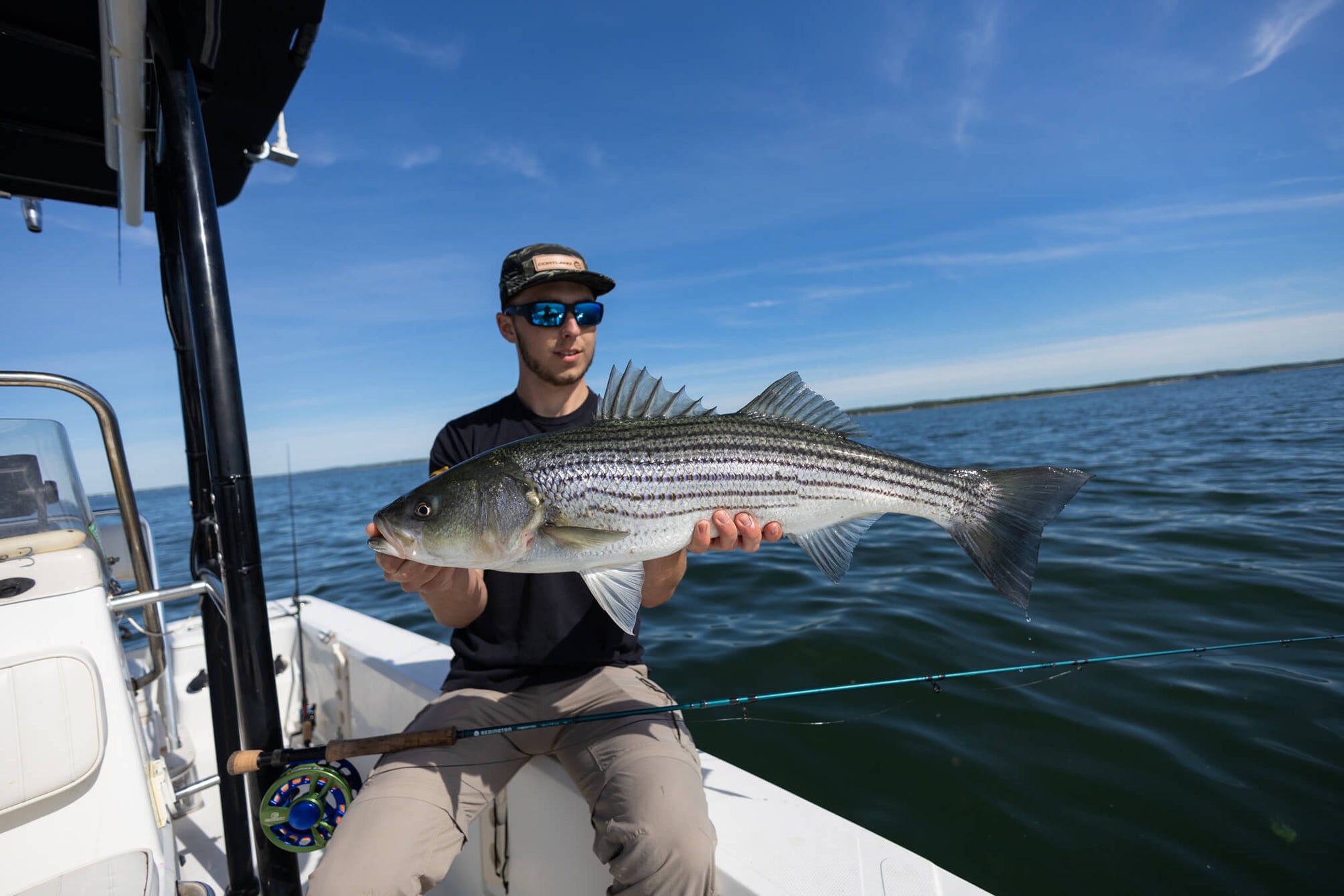 A fisherman is sitting on the edge of a boat and holding up a fish. 