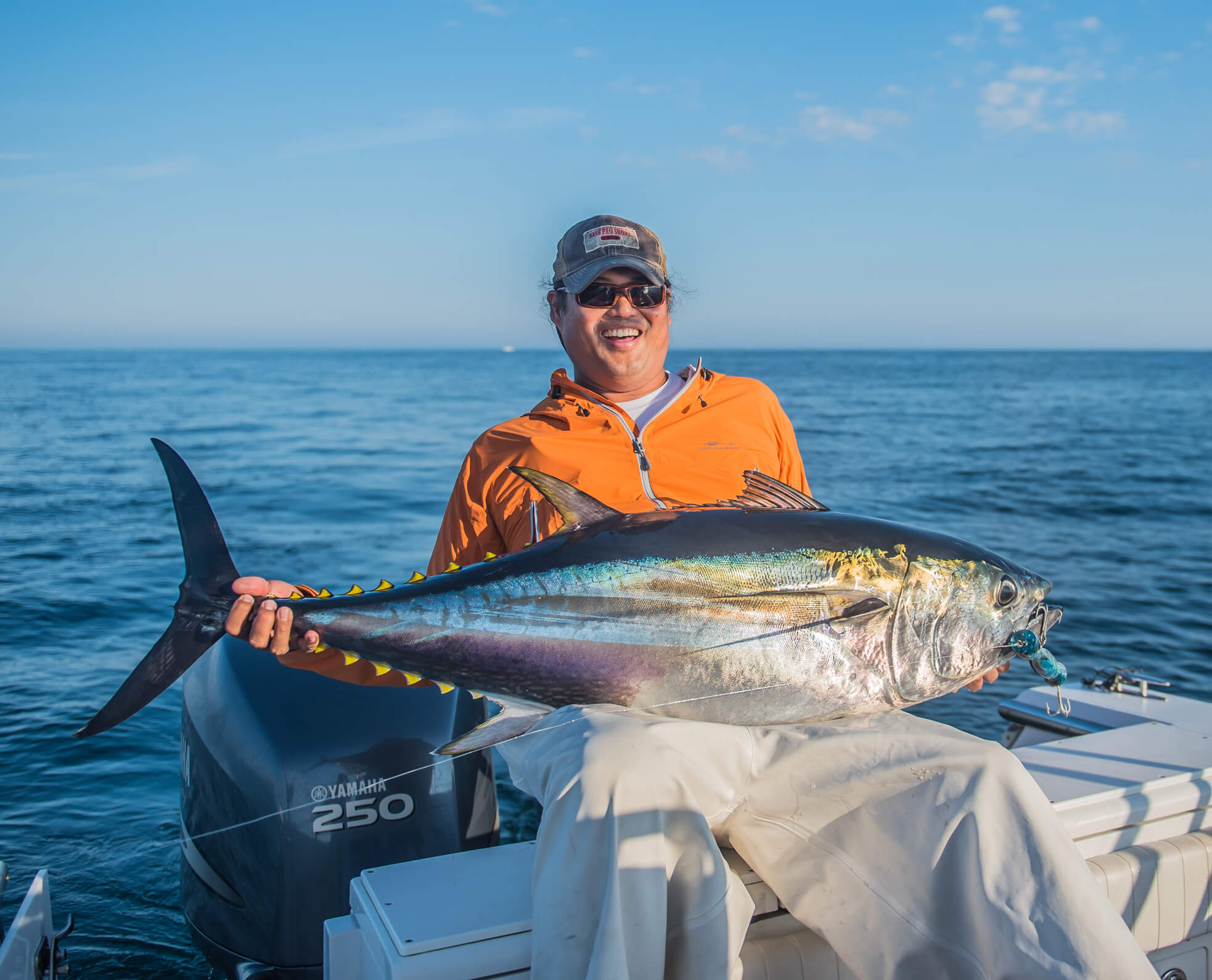 An angler is seated on a boat and has a large silver fish across his lap