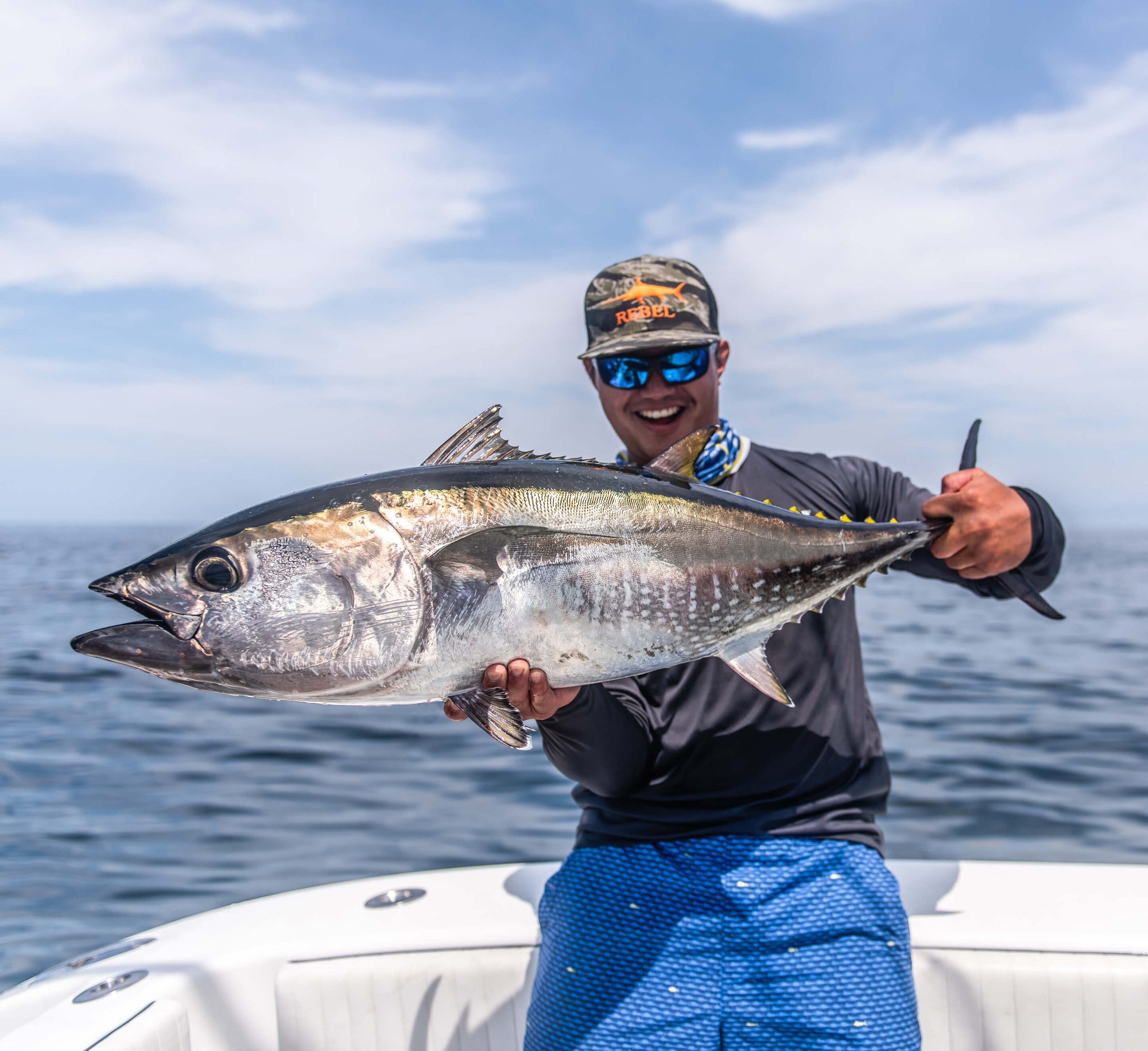 An angler is standing on a boat and holding up a silver fish