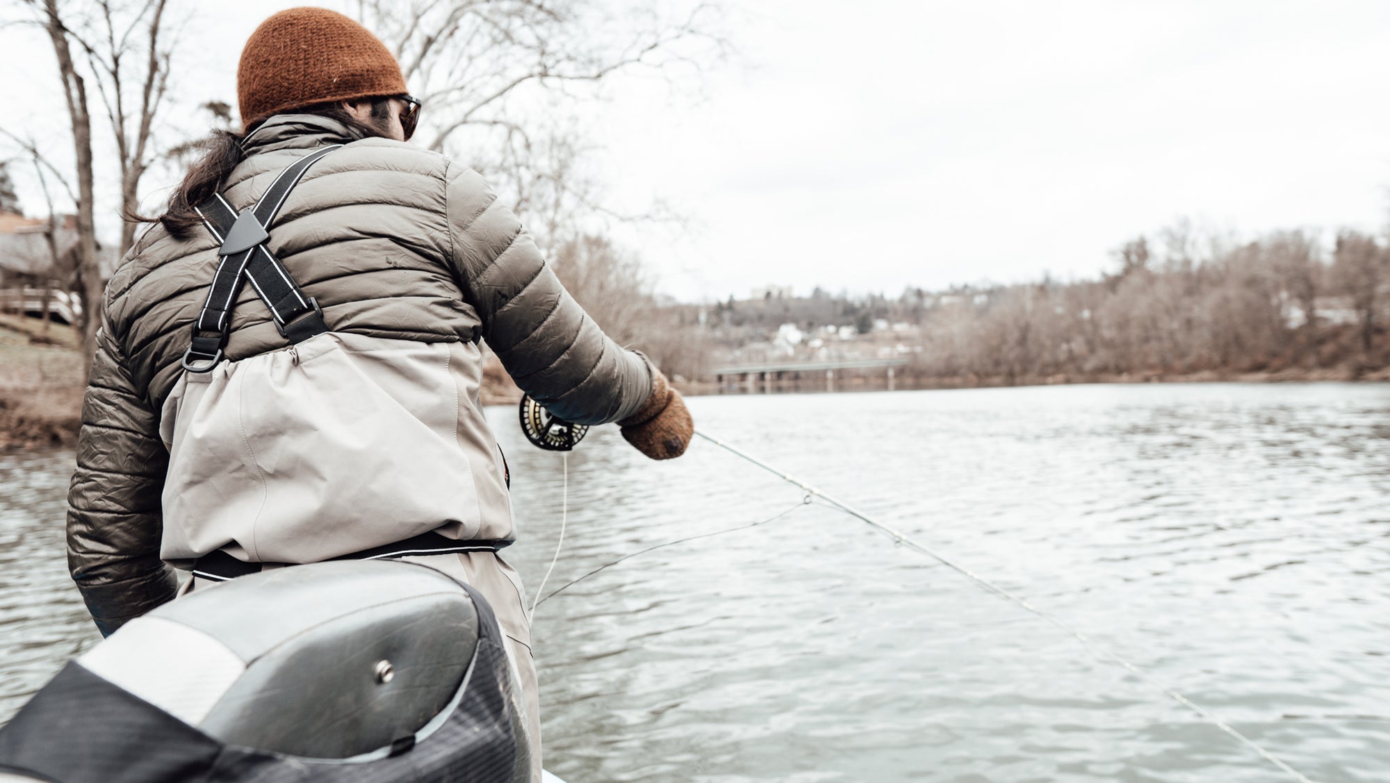 A fishman with his back turned to the camera, with his fly line cast in a body of water. 