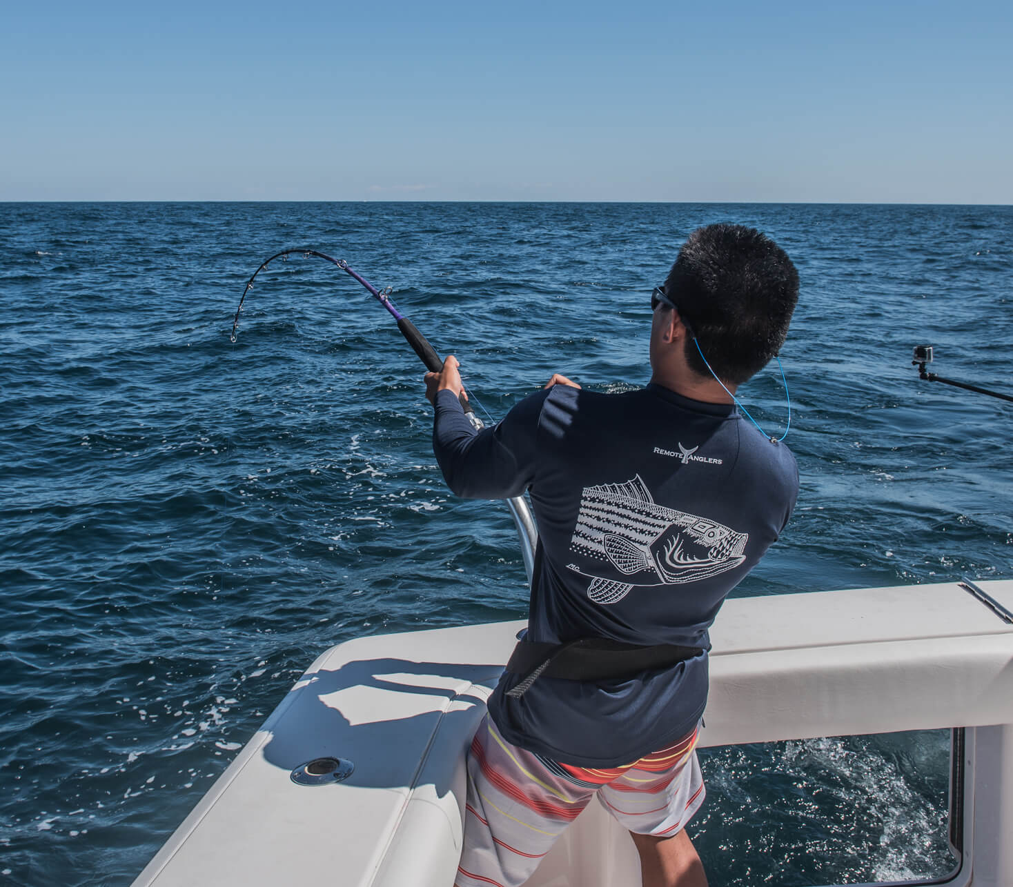 A fisherman is standing on a boat and reeling in his fishing line 