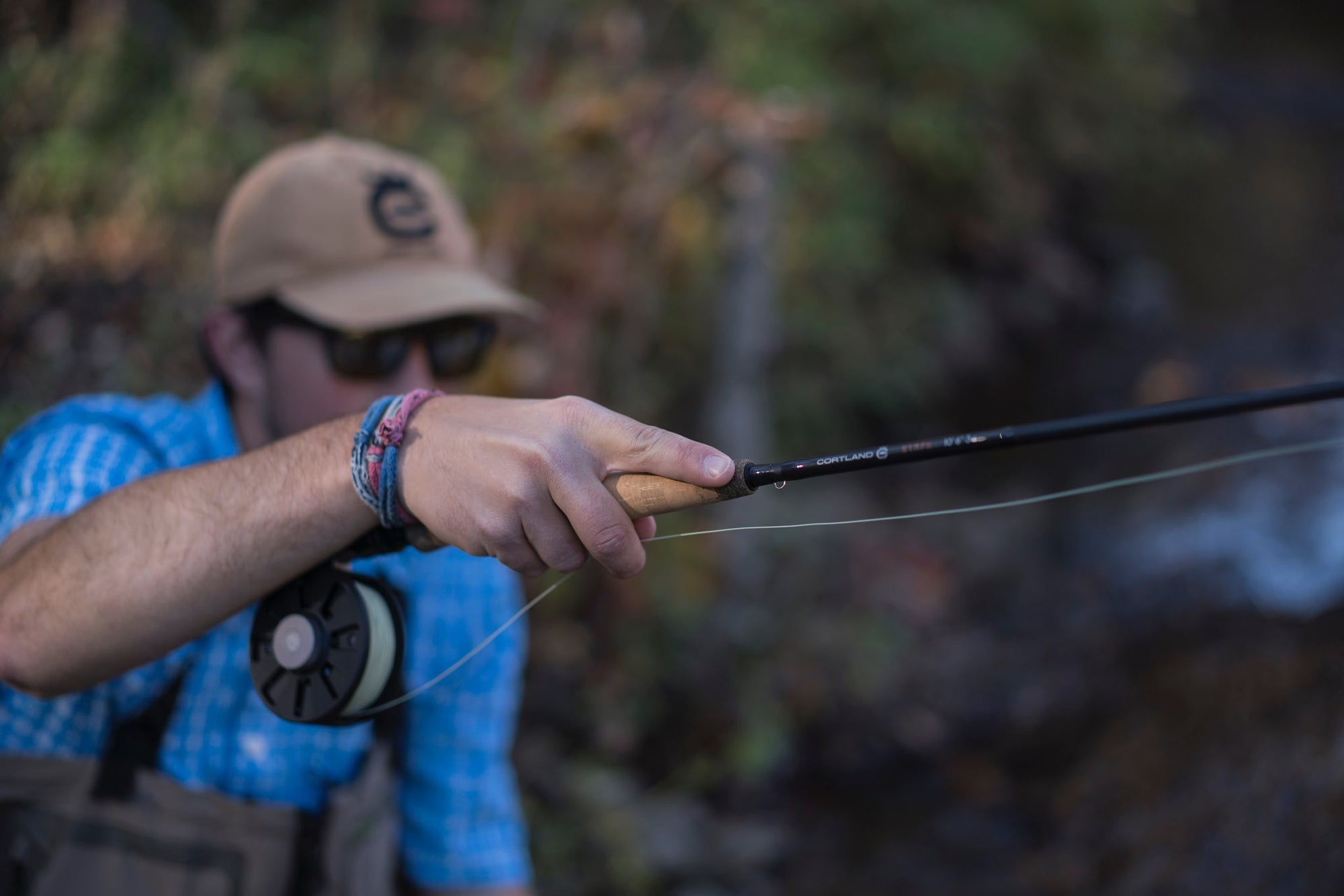 A angler in a light blue shirt holding onto a fly rod with his right hand. 